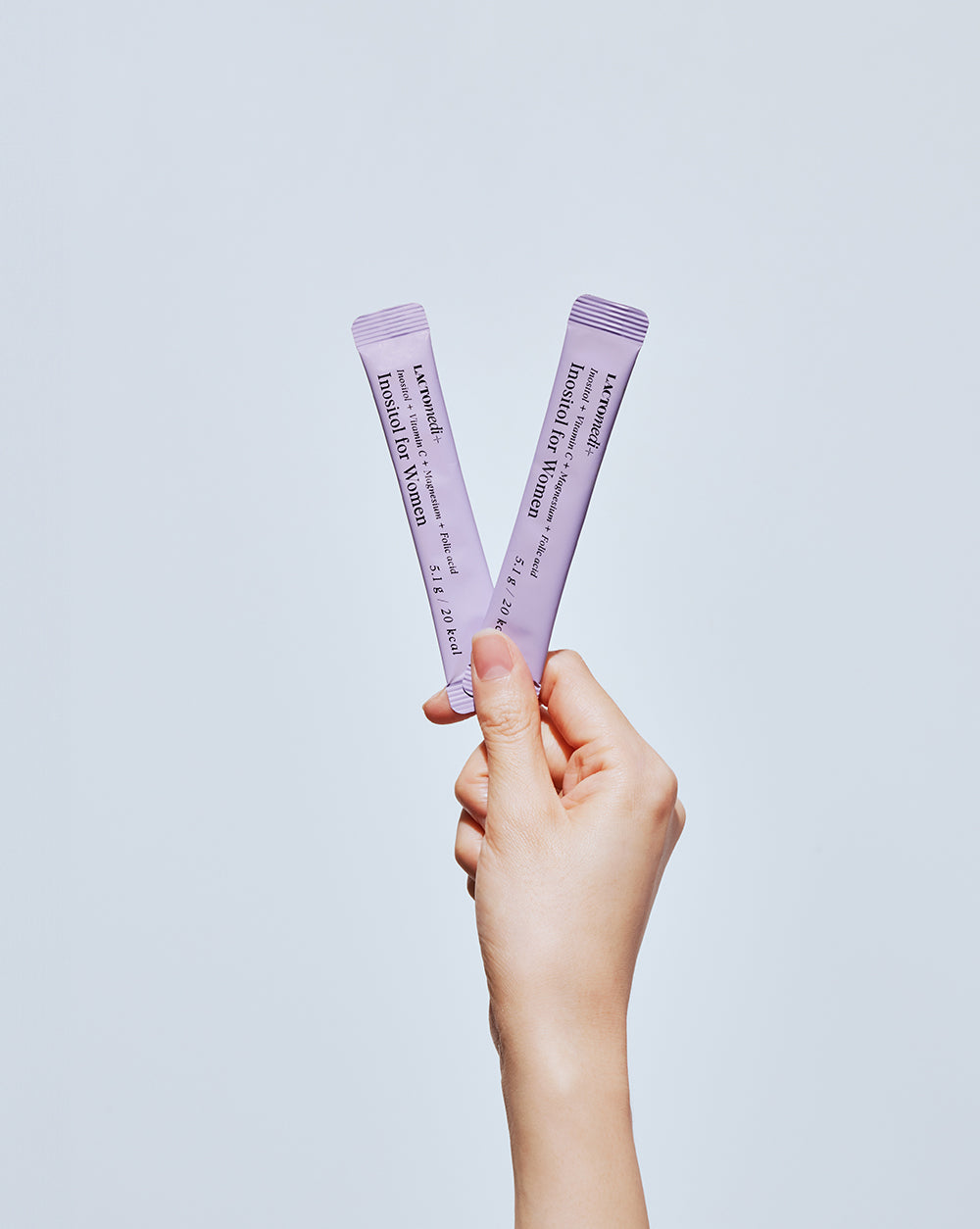 A hand holding two individual packs of Inositol for Women